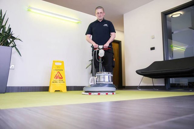 Man in Flawless Cleaning Ltd uniform washing a green office carpet