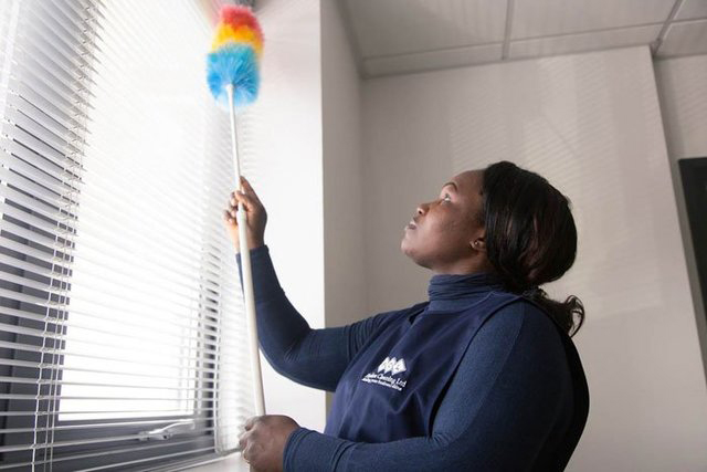 Woman with Flawless Cleaning Ltd uniform dusting window blinds